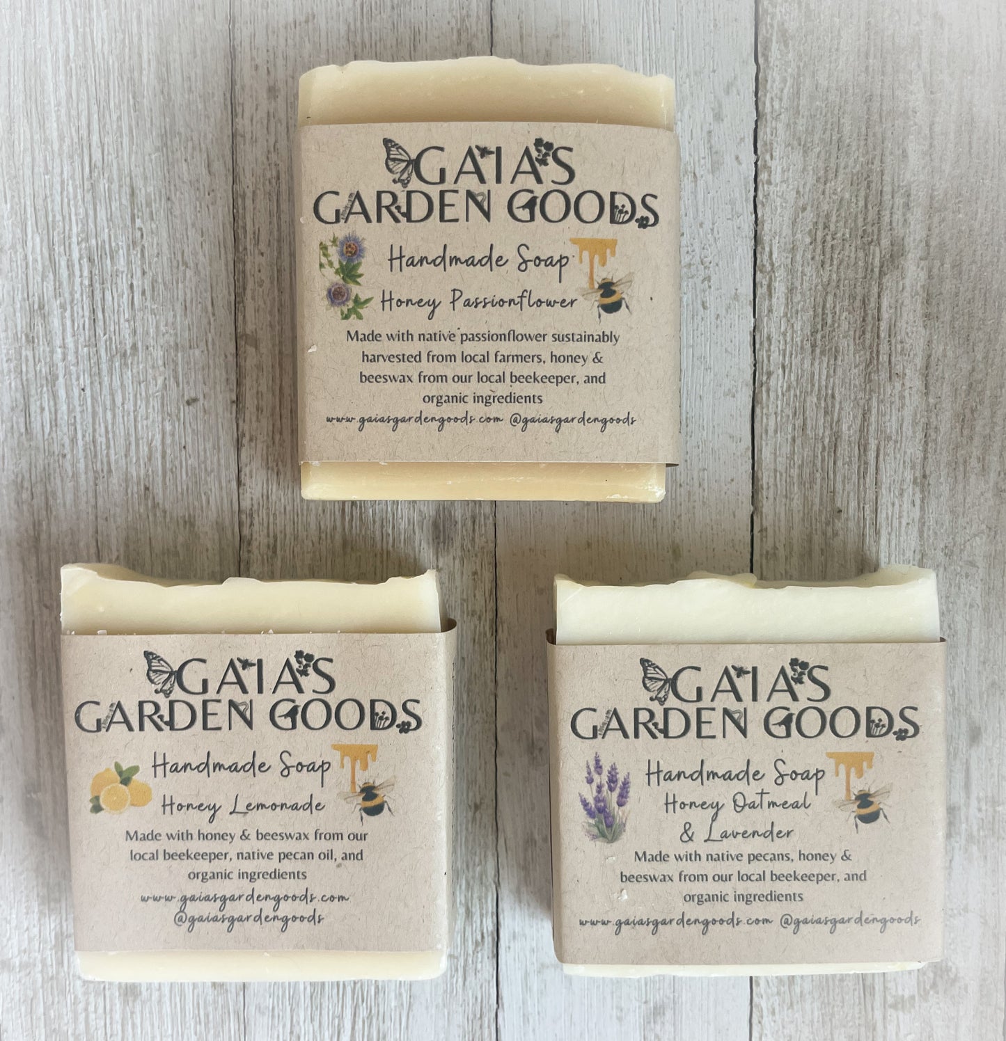 3 types of bar soaps; Honey Passionflower, Honey Lemonade, and Honey Oatmeal Lavender, lay flat against a white wood panel. The soaps are handmade with pecan oil, pecans are a native plant and great for the skin. The soaps have honeybees on the label