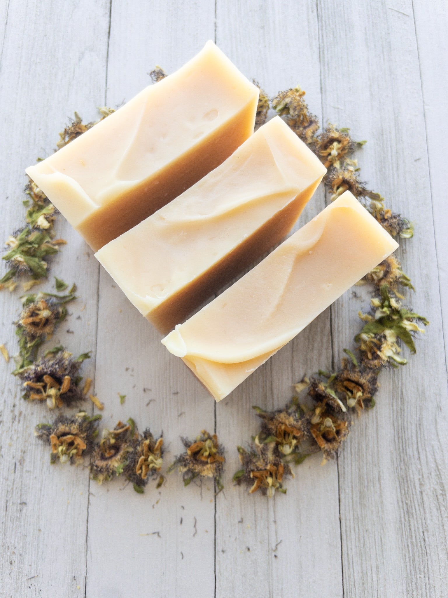 3 bars of soap stand upright. the view is of the top of the soaps. they stand in the center of a circle of dried passionflowers.